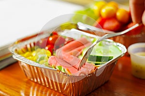 Healthy man using a fork to eat in the office a delicious mediterranean-Style fresh salad with ham on aluminium box on