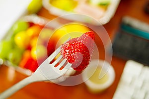 Healthy man using a white plastic fork to eat in the office a delicious raspberry with a blurred background