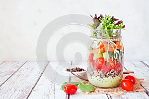 Healthy mason jar salad with vegetables and quinoa, table scene on bright background