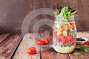 Healthy mason jar salad with vegetables and quinoa, table scene on dark background