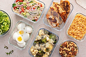 Healthy meal prep with cooked chicken breast, boiled eggs, roasted vegetables, cooked lentils, couscous salad and nuts