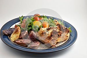 Healthy meal with roaster herb crusted chicken, multicolor fingerling potatoes, and arugula salad with heirloom tomatoes and lemon