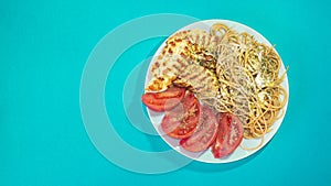 Healthy Mediterranean food in a plate filled with spaghetti, tomatoes and chicken with species in a green background.