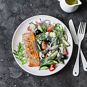 Healthy mediterranean lunch - grilled fillet salmon and vegetables, olives, feta greek salad on dark background, top view