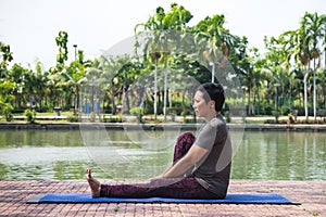 Healthy middle aged asian woman sits with knees bent at yoga exercise in the city park in the morning. healthy and lifestyle