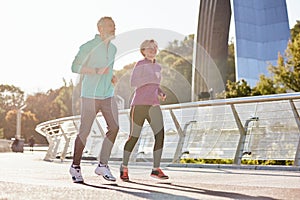 Healthy mind and body. Cheerful active mature couple in sportswear smiling while running on a sunny day. Joyful senior