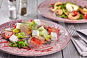 Healthy mixed Greek salad served on a pink plate with silver fork containing crisp leafy greens, microgreen, feta, onion