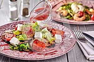 Healthy mixed Greek salad served on a pink plate with silver fork containing crisp leafy greens, microgreen, feta, onion