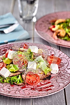 Healthy mixed Greek salad served on a pink plate with silver fork containing crisp leafy greens, microgreen, feta, onion
