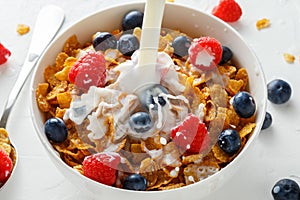 Healthy Morning Breakfast honey Corn flakes with fresh fruits of Raspberry, blueberries and pouring milk in bowl.