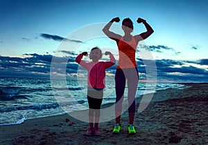 Healthy mother and child on seacoast on sunset showing biceps