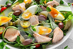 Healthy Nicoise salad with salmon, colourful sweet cherry tomatoes, olives, green beans, cucumber ribbons, soft boiled