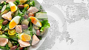 Healthy Nicoise salad with salmon, colourful sweet cherry tomatoes, olives, green beans, cucumber ribbons, soft boiled