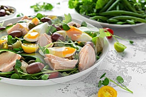 Healthy Nicoise salad with salmon, colourful sweet cherry tomatoes, olives, green beans, cucumber ribbons, soft boiled