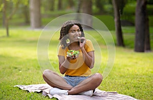 Healthy nutrition. Fit African American woman eating yummy vegetable salad from bowl at park