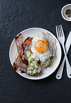 Healthy nutritious breakfast - avocado toast, bacon and fried egg on dark background