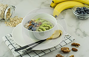 Healthy nutritious homemade food. oatmeal porridge with juicy kiwi, blueberries, nuts in a white bowl on a cloth napkin