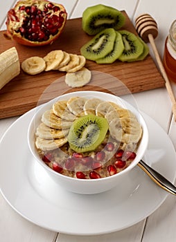 Healthy oatmeal porridge with fruits in white bowl on wooden table.
