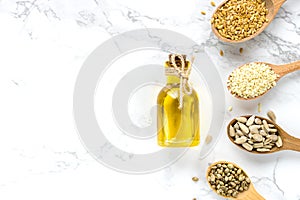 Healthy oil and sunflower seeds, flax, sesame seeds, hemp in wooden spoons on a white marble background.