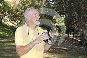 Healthy old man using binoculars to birdwatch