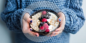 Healthy organic breakfast. Child in woolen classic blue colored sweater holding bowl of of muesli and yoghurt with fresh berries