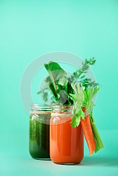 Healthy organic green and orange smoothies on blue background. Detox drinks in glass jar from vegetables - carrot
