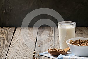 Healthy organic soy milk dairy free alternative in cup and bowl with soybean on dark wooden background. Vegan milk lactose free