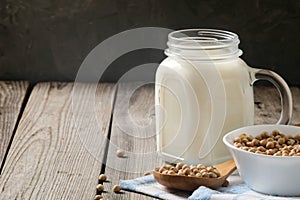 Healthy organic soy milk dairy free alternative in jar and bowl with soybean on dark wooden background. Vegan milk lactose free