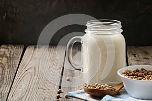 Healthy organic soy milk dairy free alternative in jar and bowl with soybean on dark wooden background. Vegan milk lactose free
