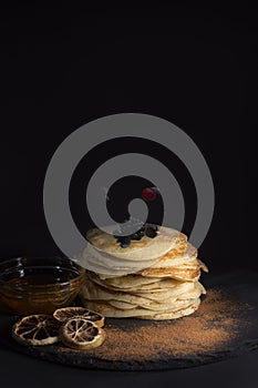 Healthy pancakes with berries and honey on black background