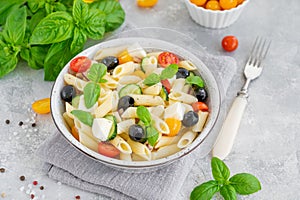 Healthy pasta salad with tomatoes, cucumbers, red onions, olives and cheese in a bowl on a gray background. Copy space