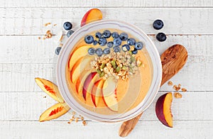 Healthy peach smoothie bowl with blueberries and granola, above view scene on white wood