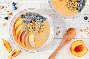 Healthy peach smoothie bowls with blueberries and granola, top view table scene on white wood