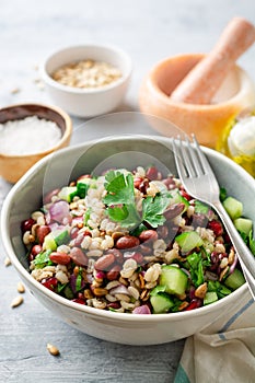 Healthy pearl barley salad with beans, cucumbers, red onion, sunflower seeds, pomegranate and parsley in bowl