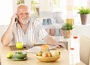 Healthy pensioner using cellphone at breakfast photo