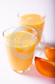 healthy persimon juice in glasses on white with two pieces of fruite at foreground