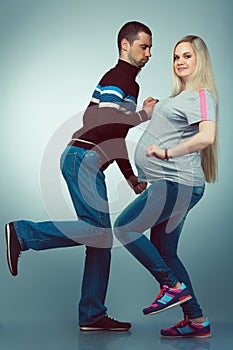 Healthy pregnancy concept. Funny full length portrait of happy husband and pregnant wife making useful exercises in trendy