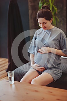 Healthy pregnancy. Young happy pregnant woman drinking clean water and gently touching belly