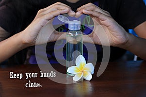 Healthy quote - keep your hands clean. With young woman hands love sign on hand sanitizer bottle and white Bali frangipani flower