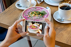 Smartphone food photography carrot soup in bowl. Woman hands take phone photo of dinner or lunch for social networks.