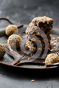 Healthy raw vegan snack. Homemade energy balls and pile of cookies with flax seeds in metal tray on black background