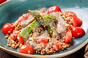 Healthy salad of barley porridge with asparagus, tomatoes and mushrooms on plate. Vegan food.