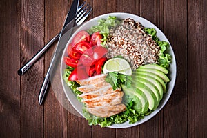 Healthy salad bowl with quinoa, tomatoes, chicken, avocado, lime and mixed greens, lettuce, parsley