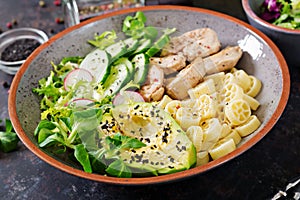 Healthy salad with chicken, avocado, cucumber, lettuce, radish and pasta on dark background. Proper nutrition. Dietary menu.