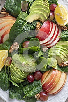 Healthy salad close up, with red apple, wallnuts, grapes and fresh spinach leaves. Dark background