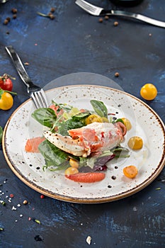 Healthy salad with crab meat, claws, grapefruit and tomatoes on white plate blue background