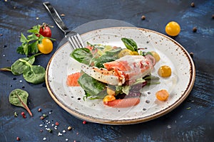 Healthy salad with crab meat, claws, grapefruit and tomatoes on white plate blue background