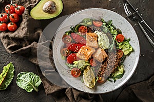 Healthy salad with fillet salmon, quinoa, avocado sauce, grilled pepper, tomatoes, lettuce, arugula in plate on wooden background