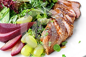 Healthy salad with medium rare beef steak, pear, grapes, lettuce, arugula, and sauce in plate isolated on white background.