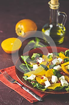 Healthy salad with persimmon, doucette lambs-lettuce, cornsalad, feld salad and feta cheese on a red plate on a red background.